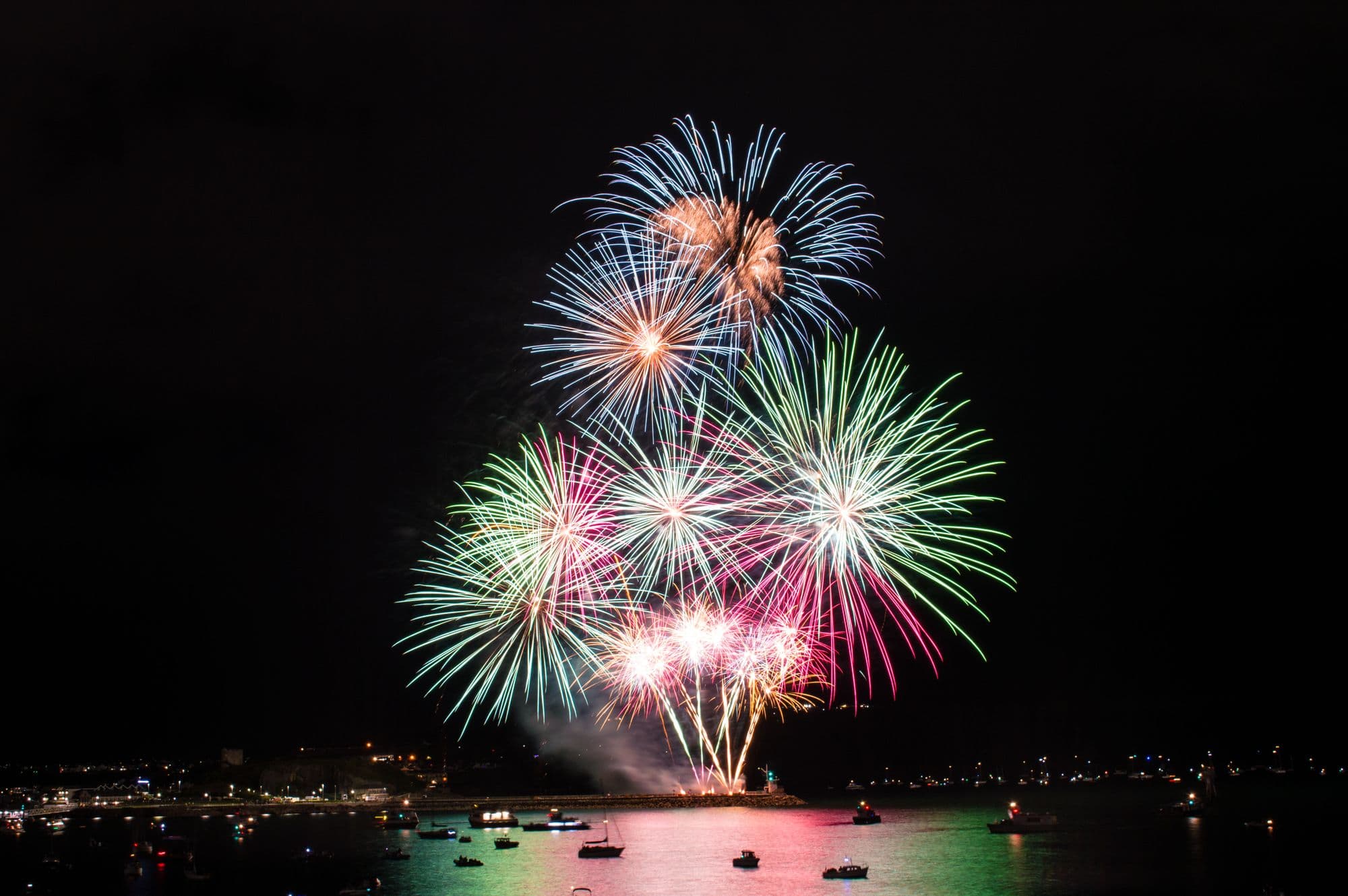 Colorful Fourth of July fireworks bursting over a harbor full of boats on the California coast at night